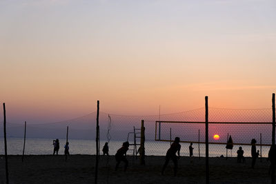 Silhouette people playing on beach against sky during sunset