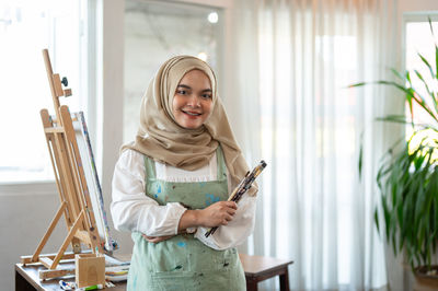 Portrait of young woman standing against window