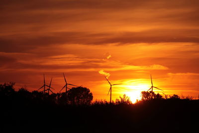 Silhouette of windmill on field against orange sky