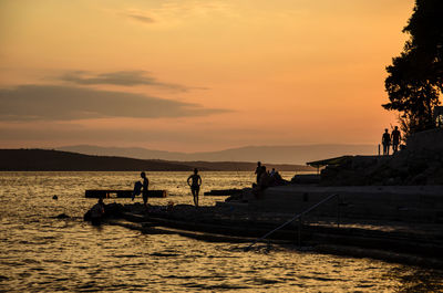 Silhouette people on sea against sky during sunset