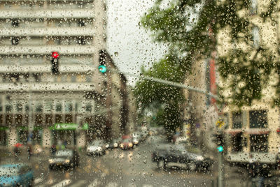 Buildings by road seen through wet window during monsoon