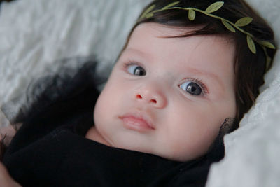 Close-up of cute baby girl wearing wreath on bed at home