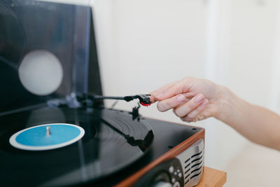 Side view of crop anonymous female turning on retro record player on shelf in house