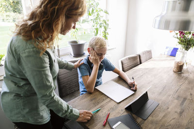 High angle view of mother looking at son studying by table