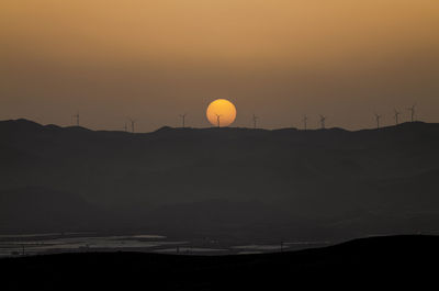 Scenic view of silhouette mountain with modern windmills against sky during sunset