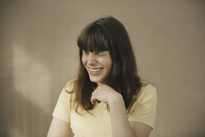 Young woman laughing against beige wall