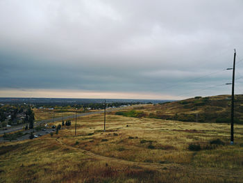 Scenic view of green landscape and sea against cloudy sky