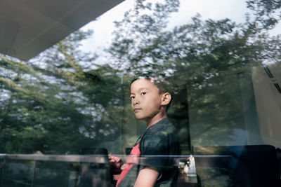 Boy looking away while standing by window