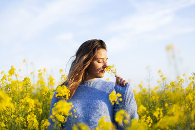 Woman smelling yellow flower on field against sky