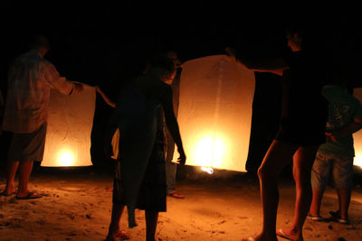 People standing against illuminated fire at night