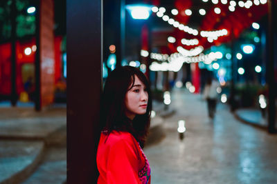 Portrait of beautiful young woman standing in illuminated city