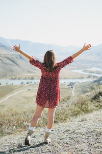 Young brunette woman in red dress on background of turquoise katun river, altai mountains