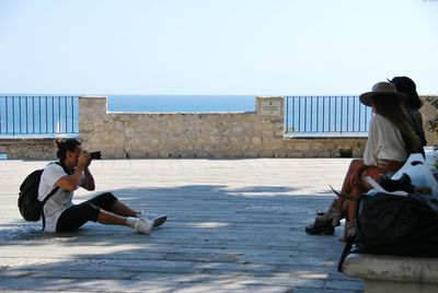 Men sitting on shore against clear sky