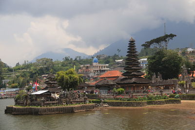 Buildings at waterfront against cloudy sky