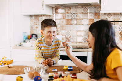 Two sisters and a brother are sitting at the table and painting easter eggs 