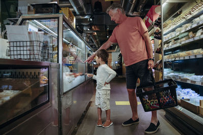 Senior man showing food to grandson in display while shopping at supermarket