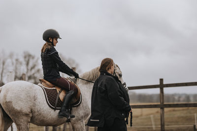 Girl horseback riding with female instructor walking along her