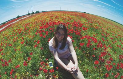 Portrait of beautiful woman sitting amidst red poppies on field