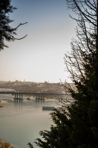 Bridge over river by buildings in city against sky at sunset