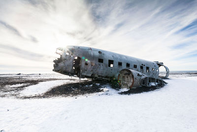 Abandoned airplane crash on snowy field against sky during sunset