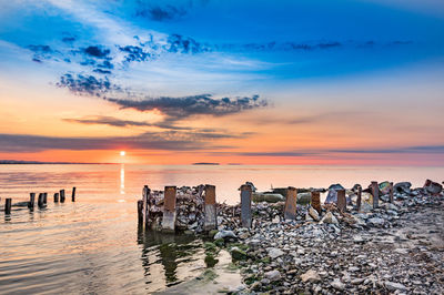 Wooden posts on beach against sky during sunset