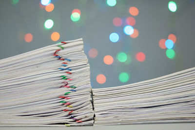 Close-up of paper stacked on table against blurred lights