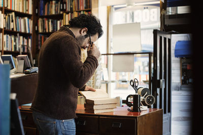 Owner holding eyeglasses while reading book in library