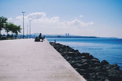 People on groyne at sea against sky