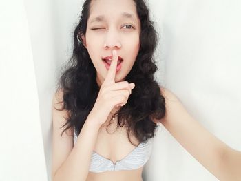 Portrait of young woman with finger on lips against white background