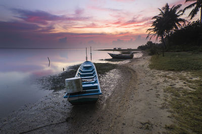 Boats moored on beach against sky during sunset