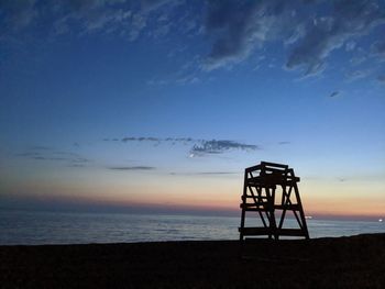 Silhouette lifeguard hut on beach against sky during sunset