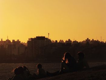 Silhouette people sitting by sea against clear sky during sunset