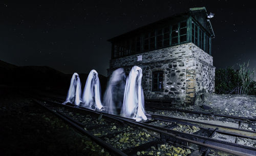 Statue by railroad tracks against building at night