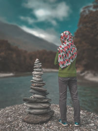 Rear view of woman standing by stones stacked at riverbank