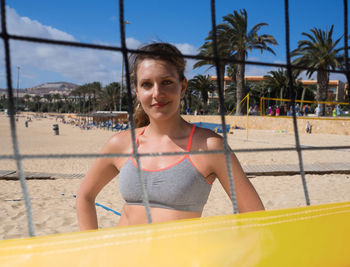 Woman seen through net at beach against blue sky