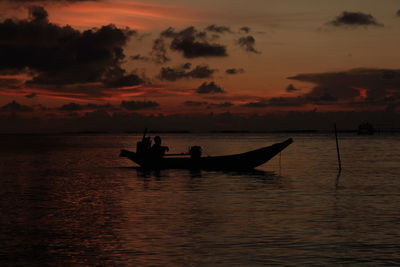 Silhouette people in sea against sky during sunset