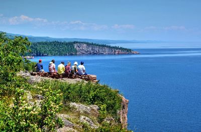 Rear view of friends sitting at palisade head peak while looking at lake superior