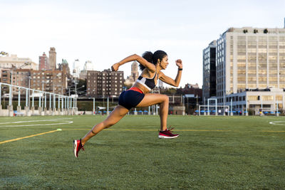 Side view of female athlete running on grassy field against sky