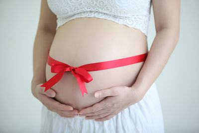 Midsection of pregnant woman with ribbon standing against gray background