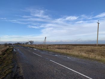 Country road by field against sky