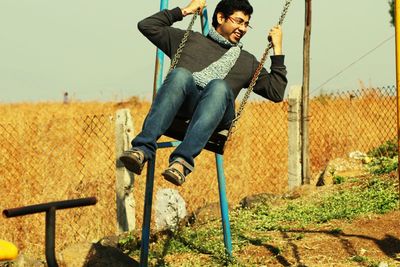 Full length of smiling young man swinging against clear sky during sunny day