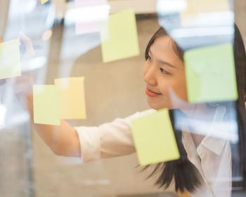 Businesswoman writing on adhesive note seen through glass at office