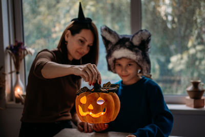 Mom and son in halloween costumes play together with jack-o-lantern spooky pumpkins lamp at home