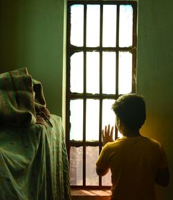 Rear view of man standing by window at home