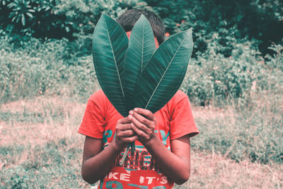 Boy holding leaves while standing on field