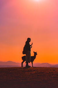 Silhouette men sitting on land against sky during sunset