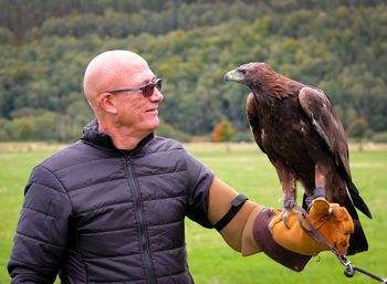 Senior man holding eagle while standing against trees in forest