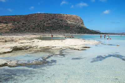 Group of people on rocks at beach against sky