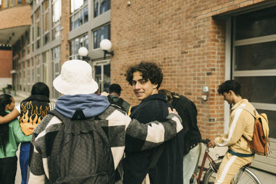 Smiling teenage boy looking over shoulder while walking with friends on sidewalk