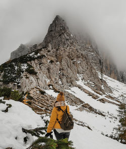 Rear view of female hiker on snowy path leading to amazing misty rocky mountain